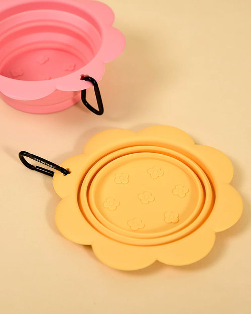 Pink and yellow collapsible flower-shaped silicone pet bowls shown open and folded on a tan background