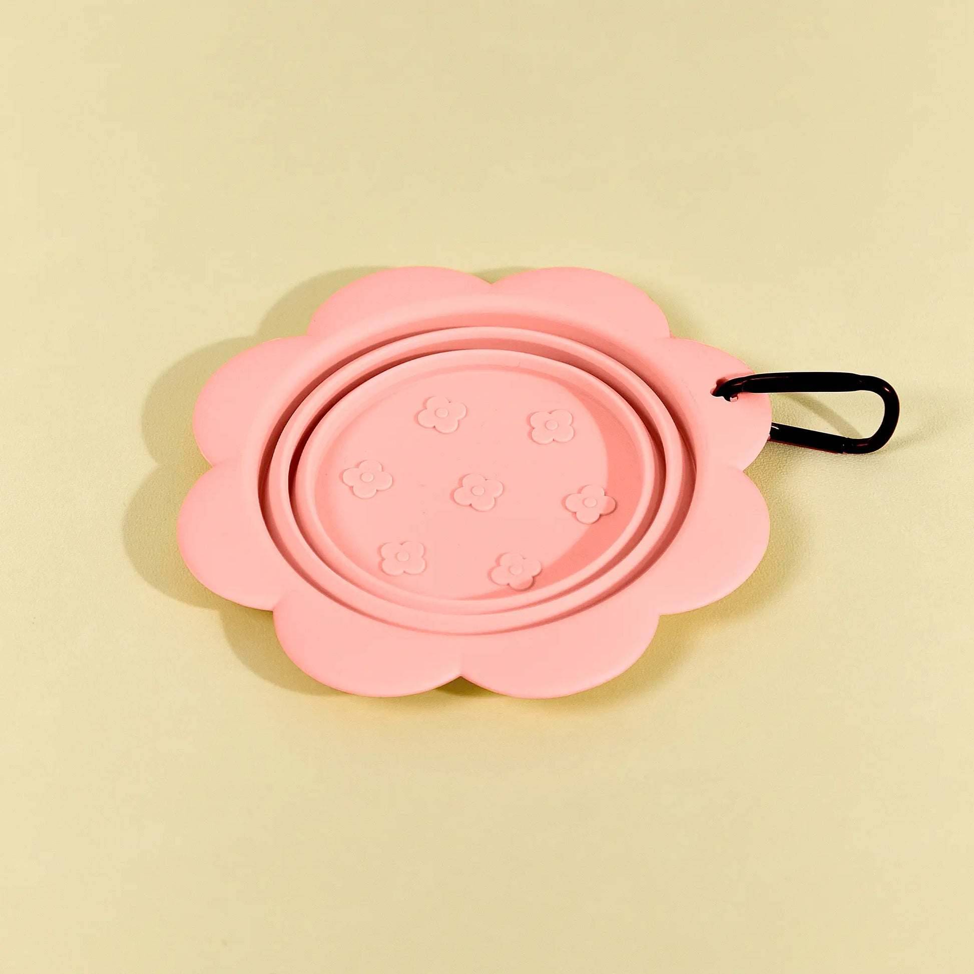 Pink collapsible flower pet bowl shown folded completely flat with a carabiner clip attached