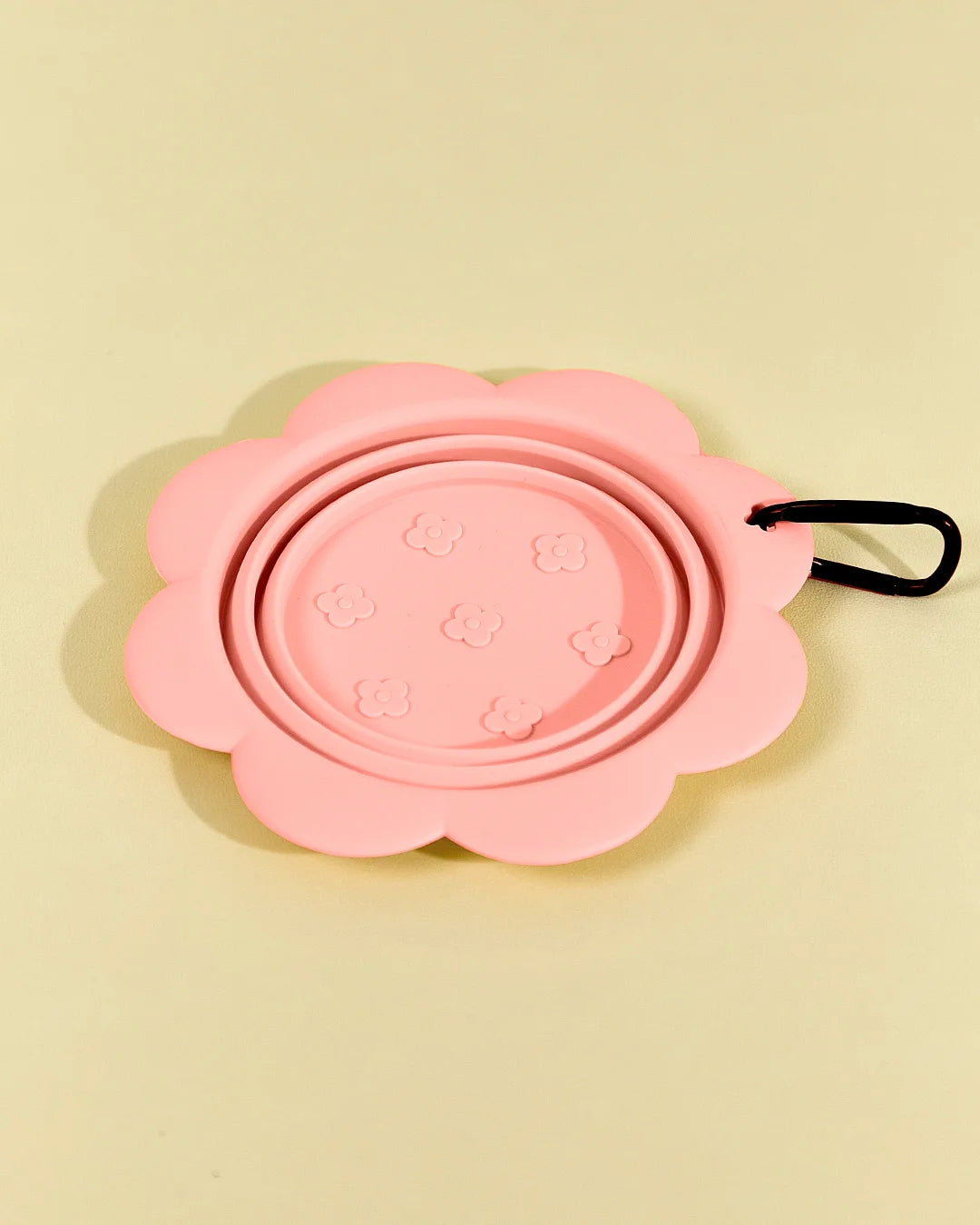 Pink collapsible flower pet bowl shown folded completely flat with a carabiner clip attached