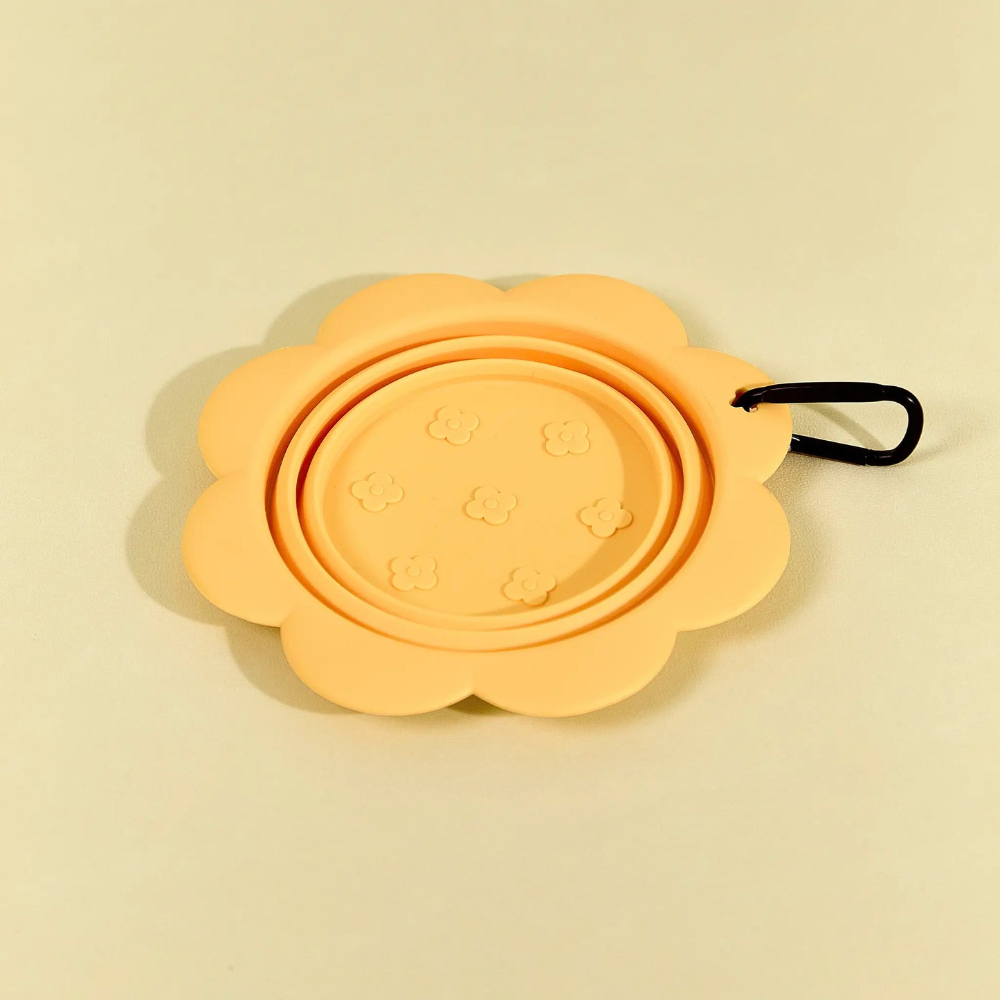 Yellow collapsible flower pet bowl shown folded completely flat with a carabiner clip attached