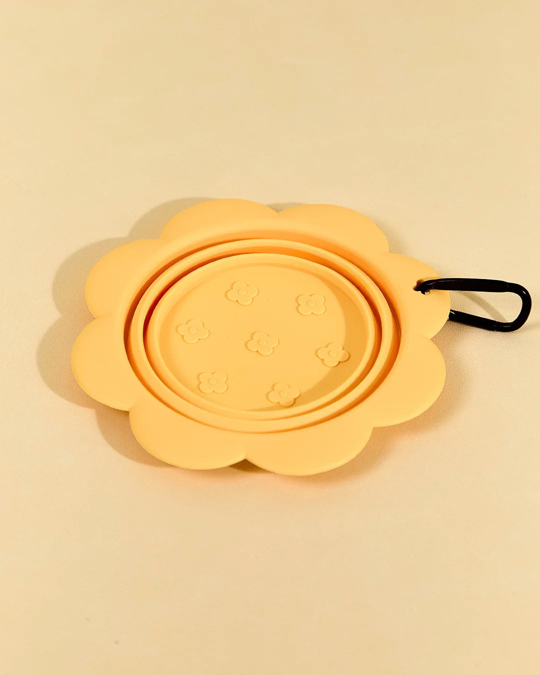 Yellow collapsible flower pet bowl shown folded completely flat with a carabiner clip attached