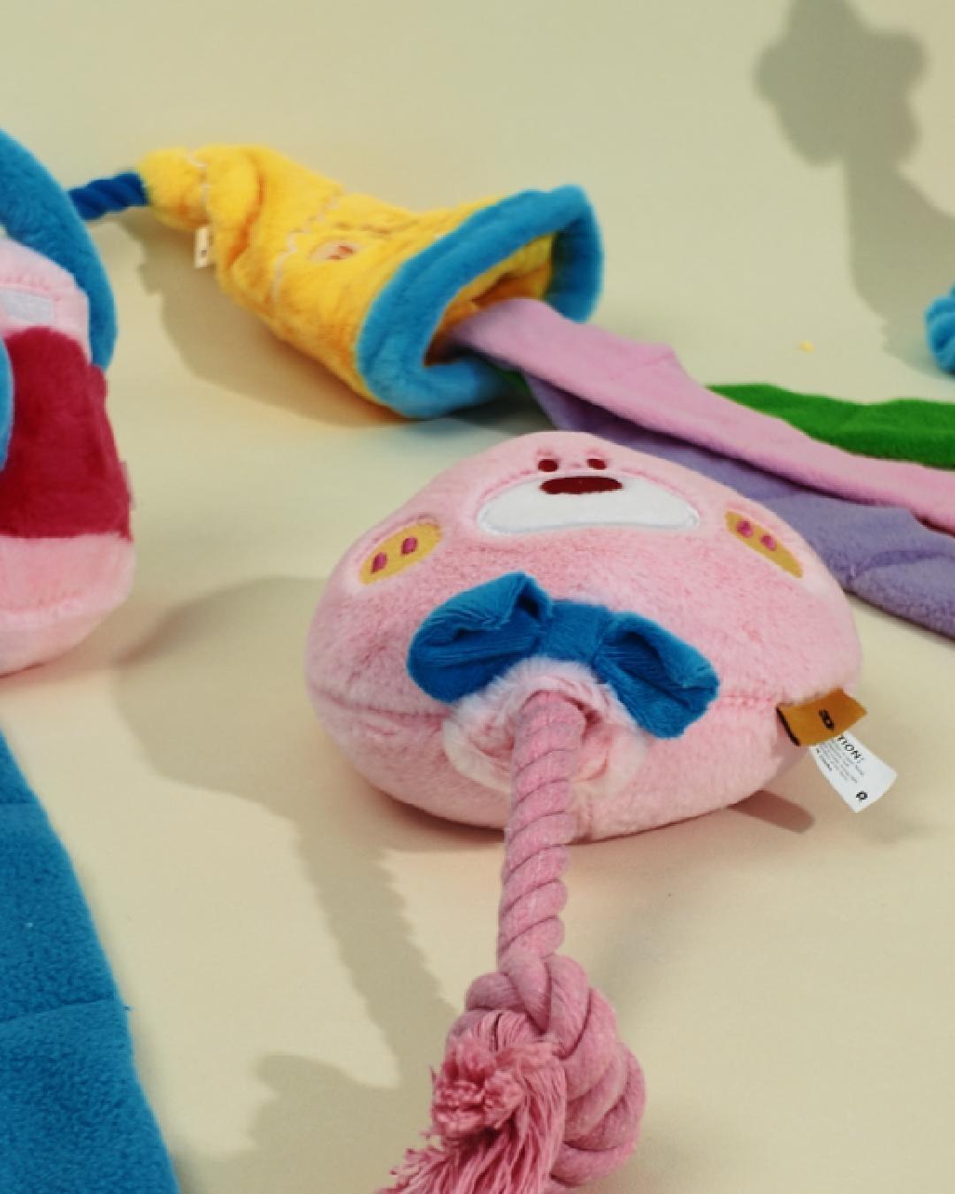 A camera-shaped plush dog toy and pink squeaky toy displayed on a clean background next to a Miniature Schnauzer playing on a sofa.