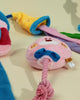 A camera-shaped plush dog toy and pink squeaky toy displayed on a clean background next to a Miniature Schnauzer playing on a sofa.