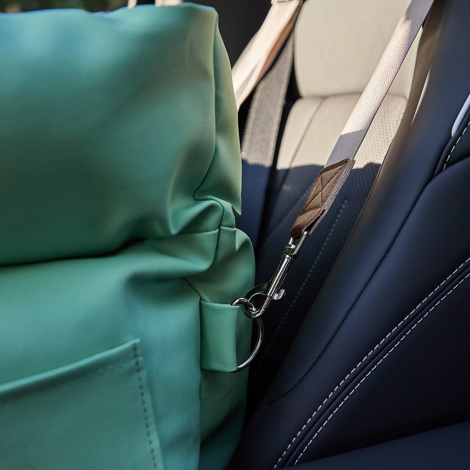 Detail of a standard car seatbelt threaded through the back straps of the dog seat to ensure steady stability for traveling pets.