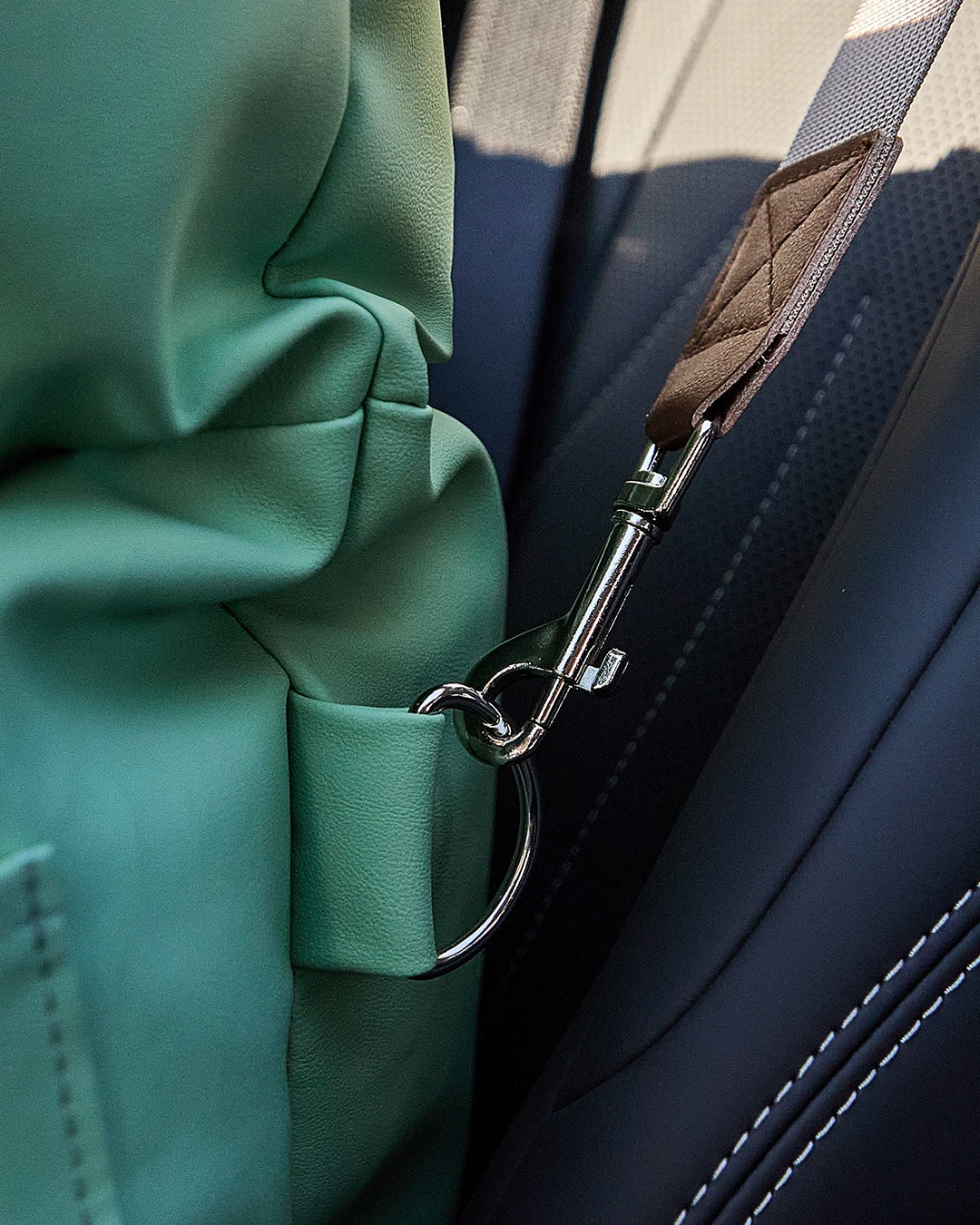 Detail of a standard car seatbelt threaded through the back straps of the dog seat to ensure steady stability for traveling pets.